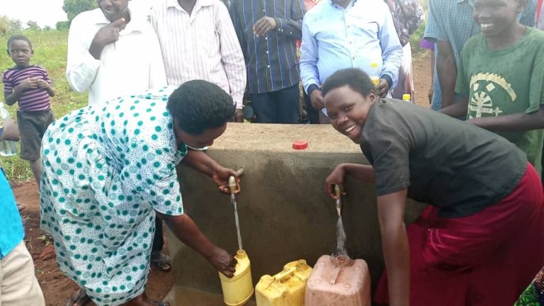 Two women in front of faucets filling jugs with water