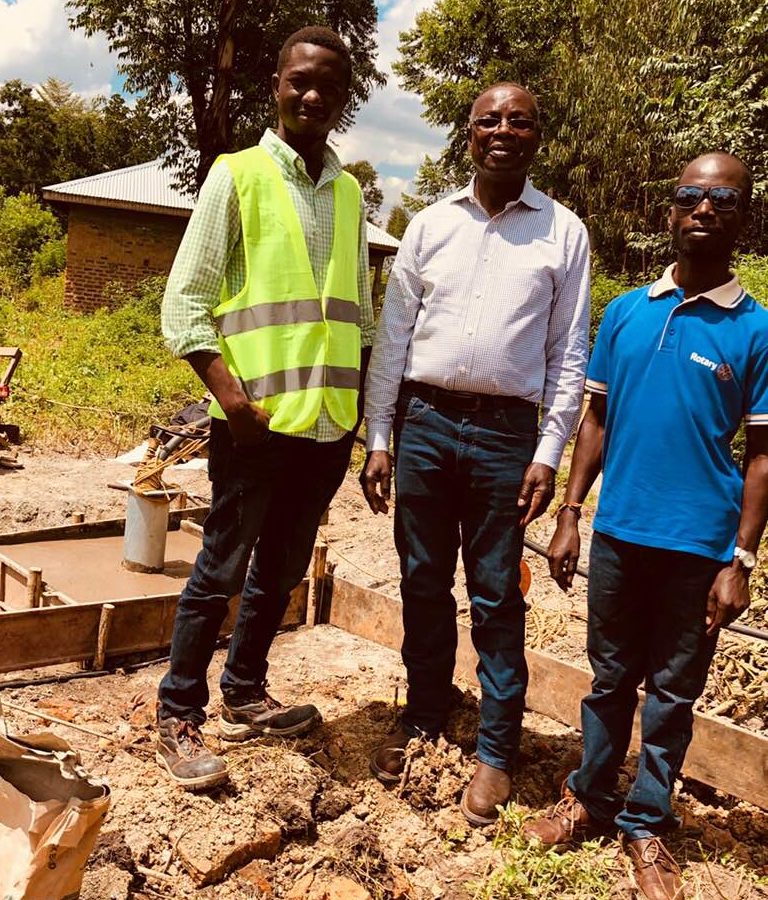 Three men standing on muddy ground in front of trees