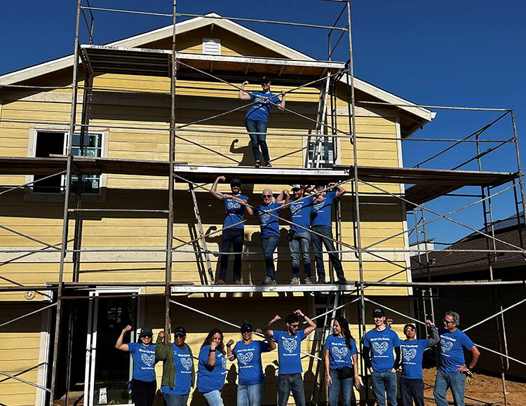 People in blue shirts standing on scaffolding in front of a house
