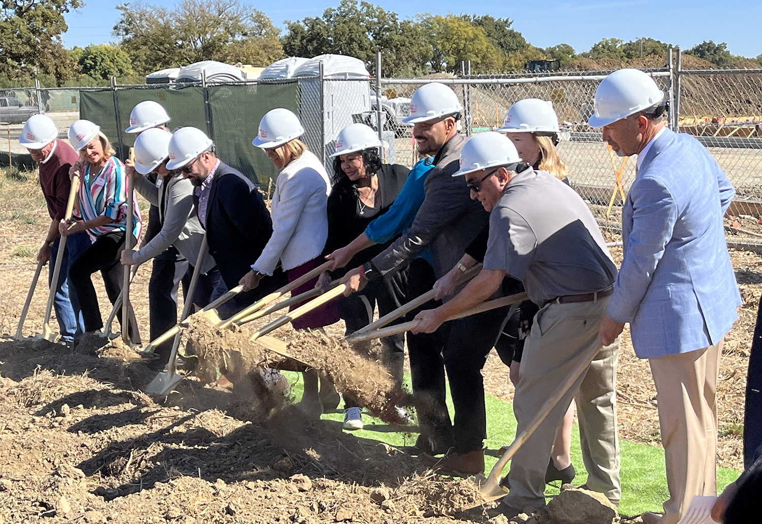 Eight people wearing hard hats digging with shovels