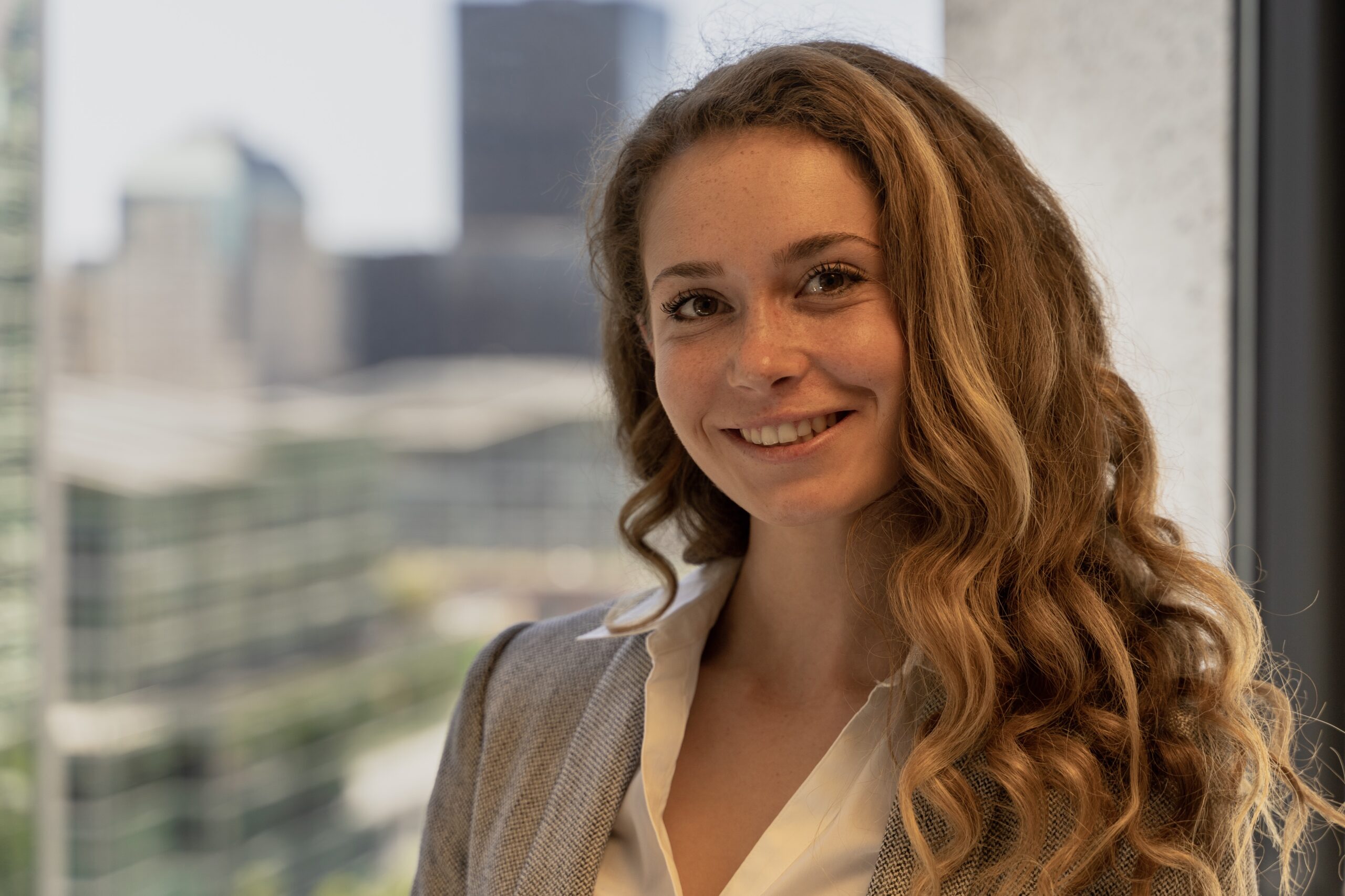 Woman with curly red hair wearing a white colored shirt in front of a window